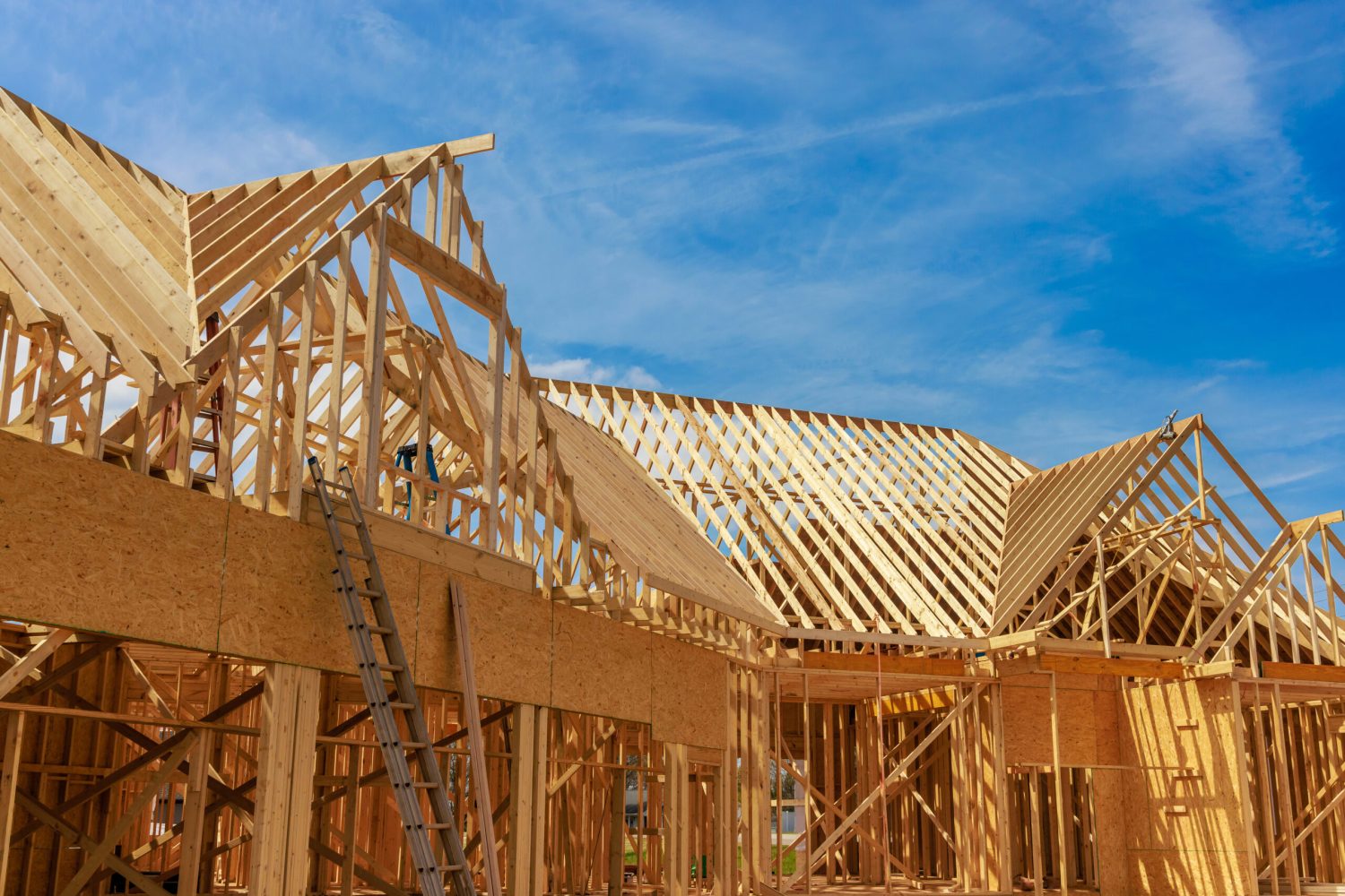 Wood roof framing beams of a house under construction against a blue sky